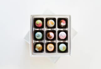 A box of nine beautifully crafted chocolates in various colors and designs.
