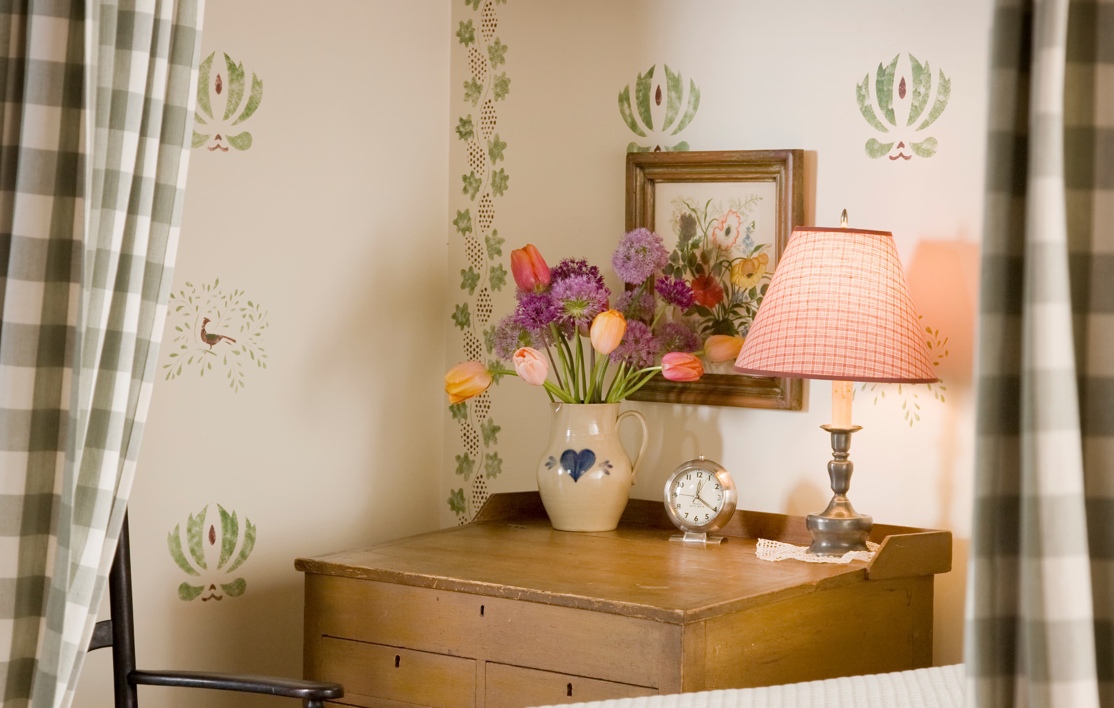 A bedroom detail featuring a wooden nightstand with a lamp and a vase of purple tulips