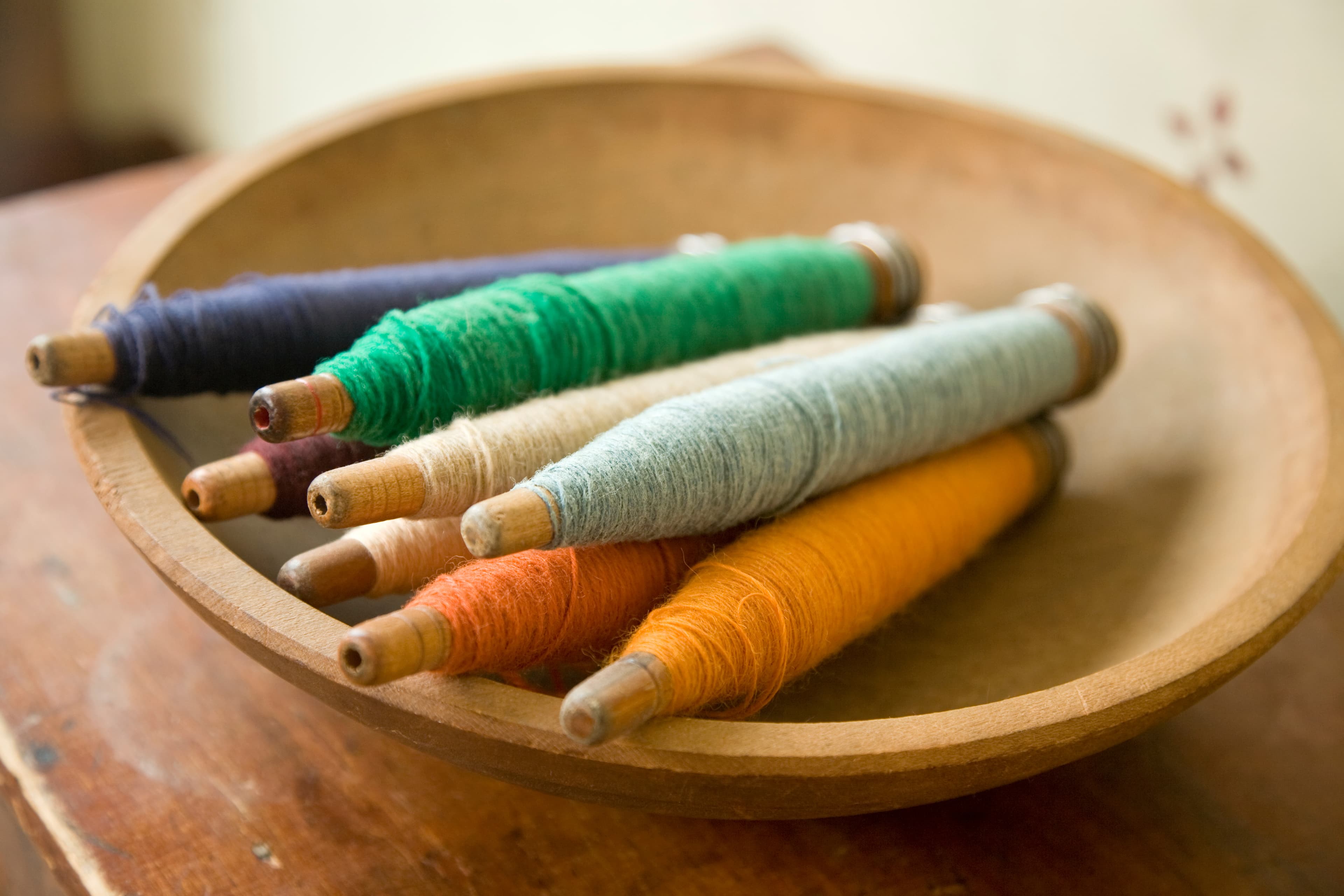 A wooden bowl filled with colorful spools of thread in various shades.
