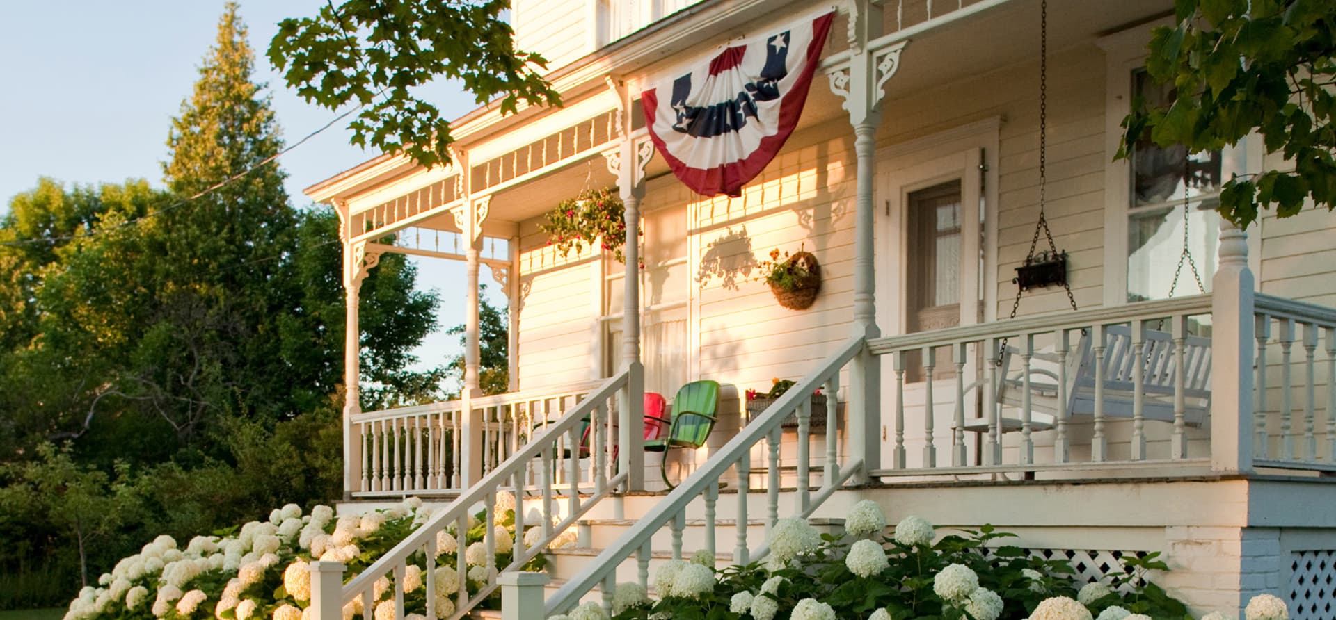 A charming white-clapboard house with a decorated porch and hydrangeas in full bloom.