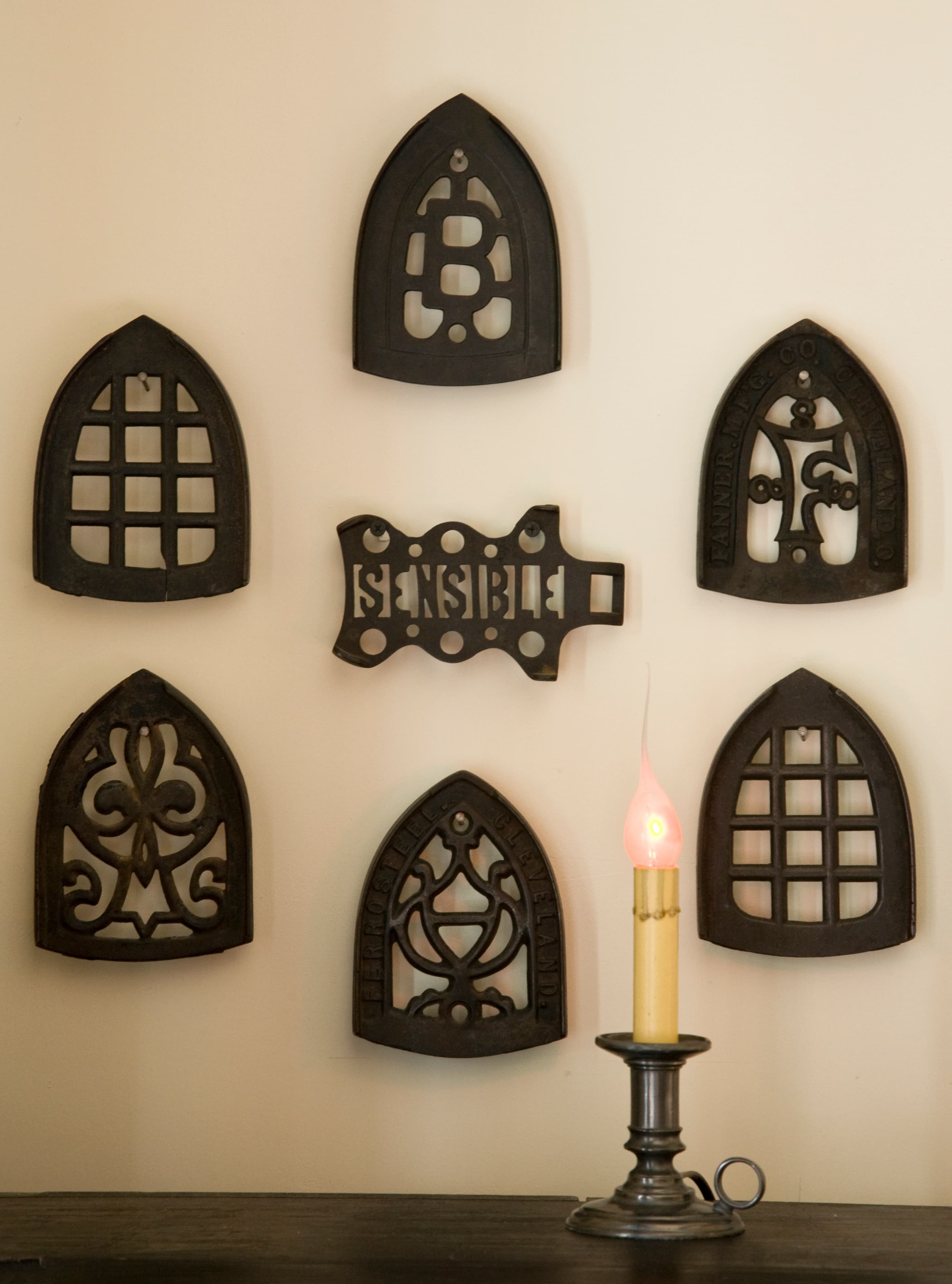 A collection of decorative Gothic-style iron wall panels arranged above a candle holder with a lit candle.