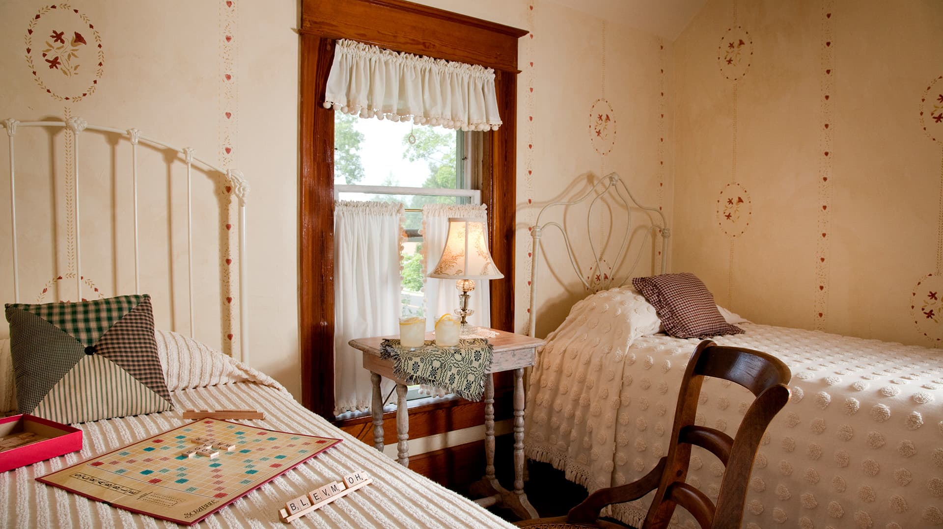 A cozy bedroom featuring two twin beds, a wooden chair, and a small table with a lamp.