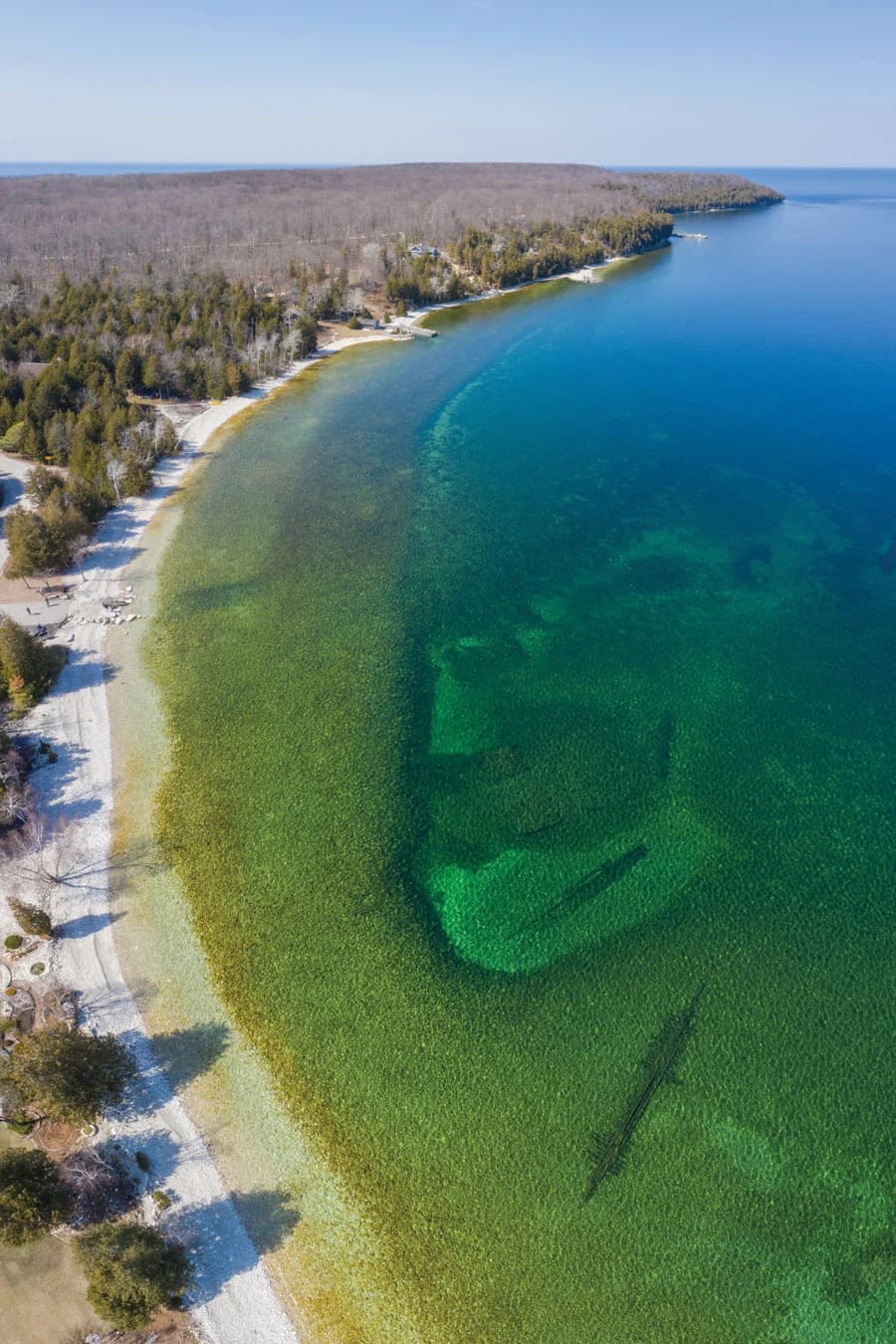 Aerial view of a clear, turquoise coastline bordered by trees and sandy shores.