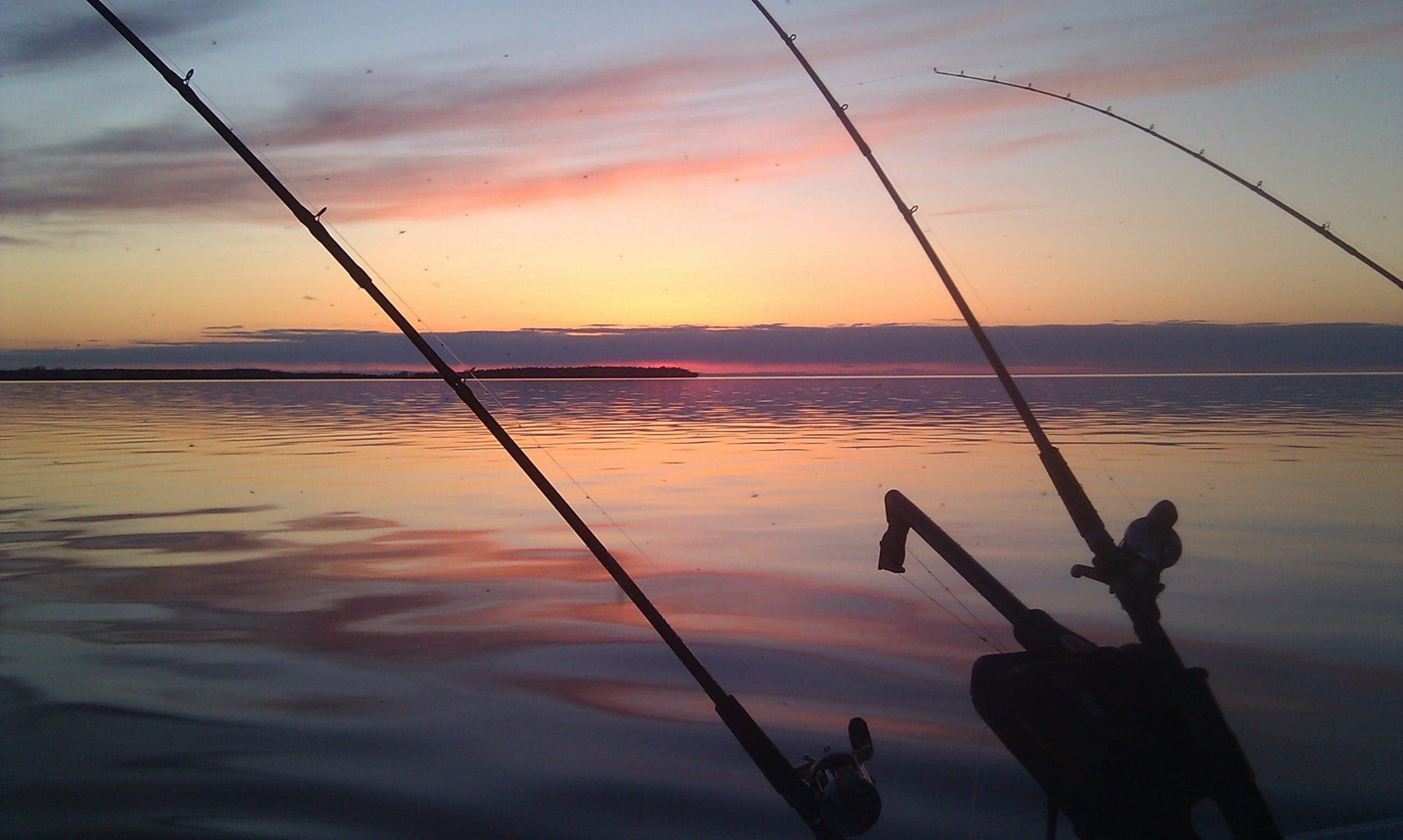 Two fishing rods silhouetted against a colorful sunset over calm water.