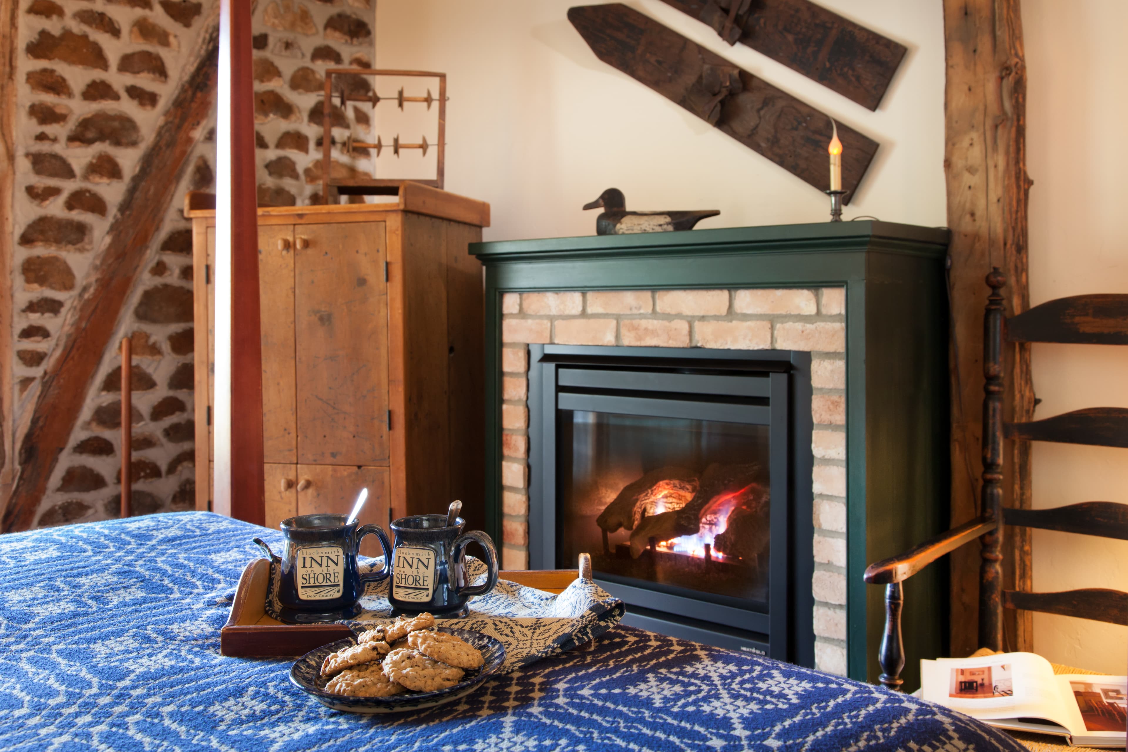 A cozy bedroom with a fireplace, a tray of cookies, and two mugs on the bed.