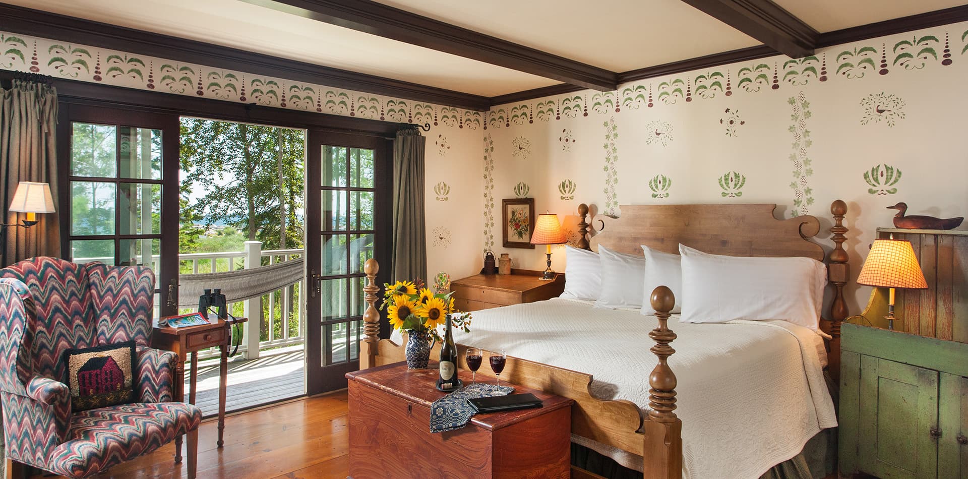A cozy bedroom featuring a wooden bed, patterned armchair, and large windows overlooking a scenic view.
