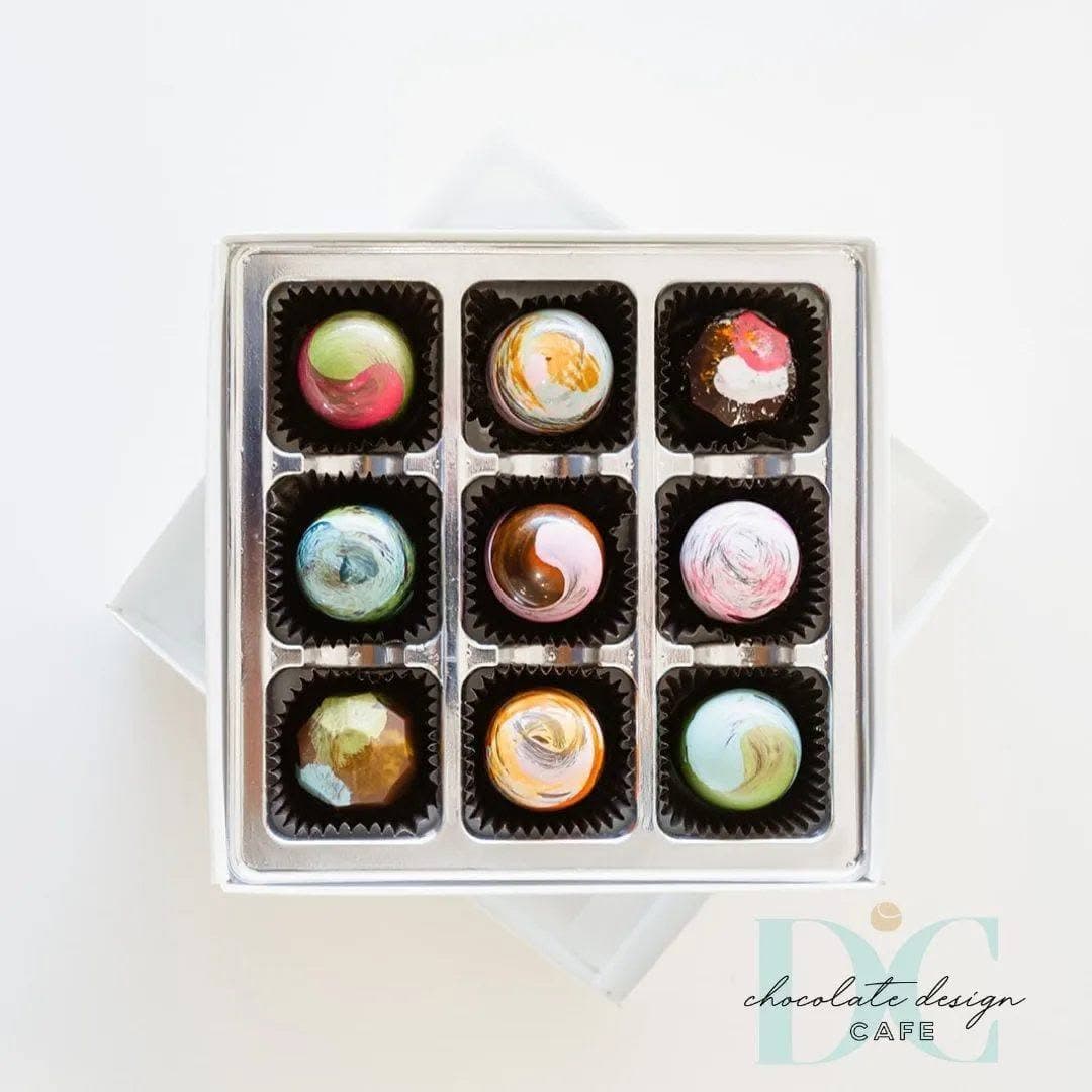 A box of nine colorful, decorative chocolates arranged in a grid.