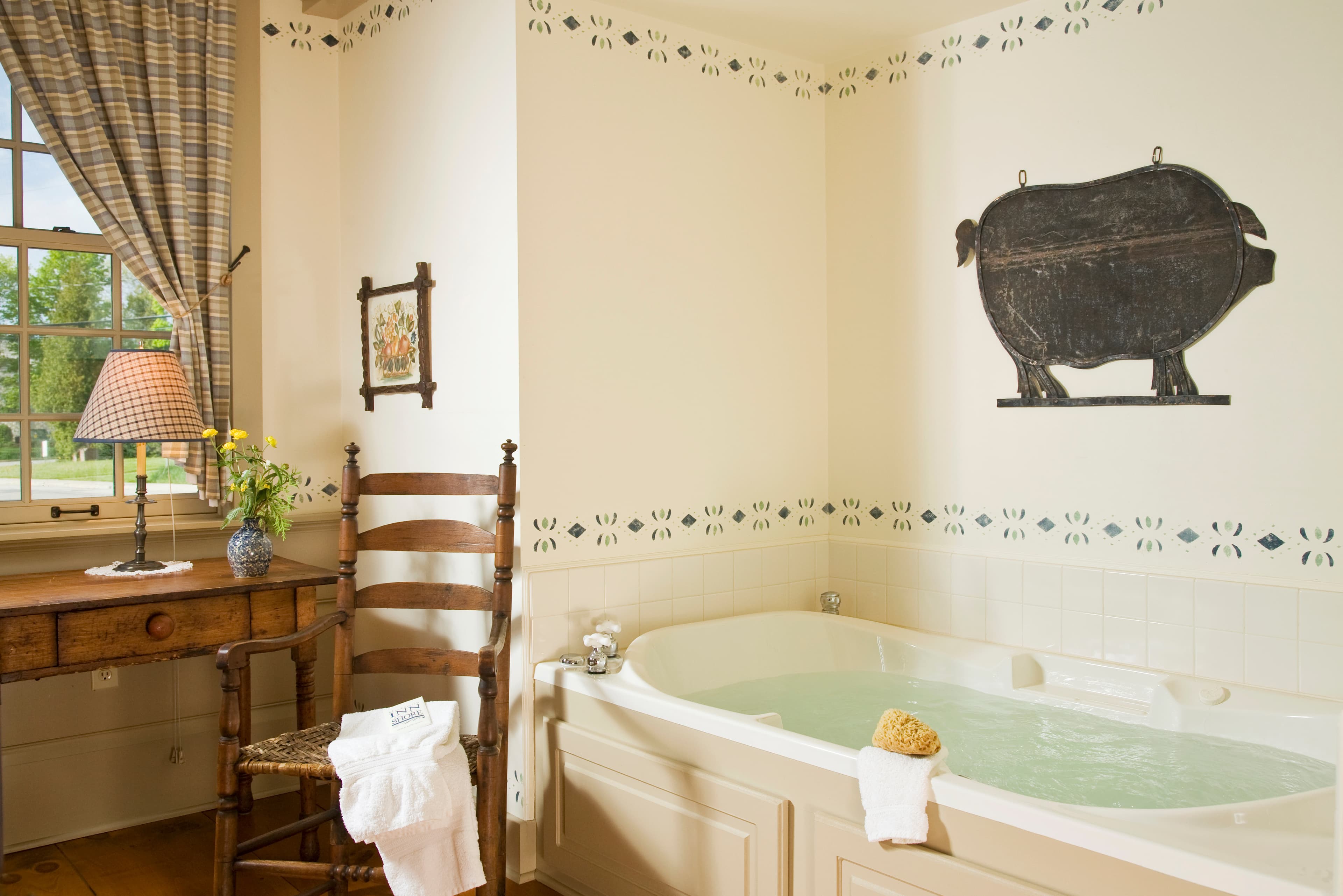 A cozy bathroom featuring a large tub, a wooden chair, a decorative lamp, and floral accents.