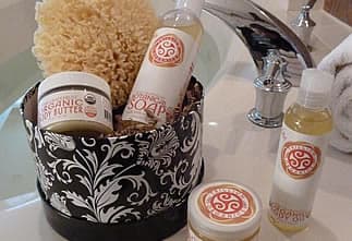 A decorative basket contains organic soap, butter, and a natural sponge, placed near a sink in a bathroom setting.