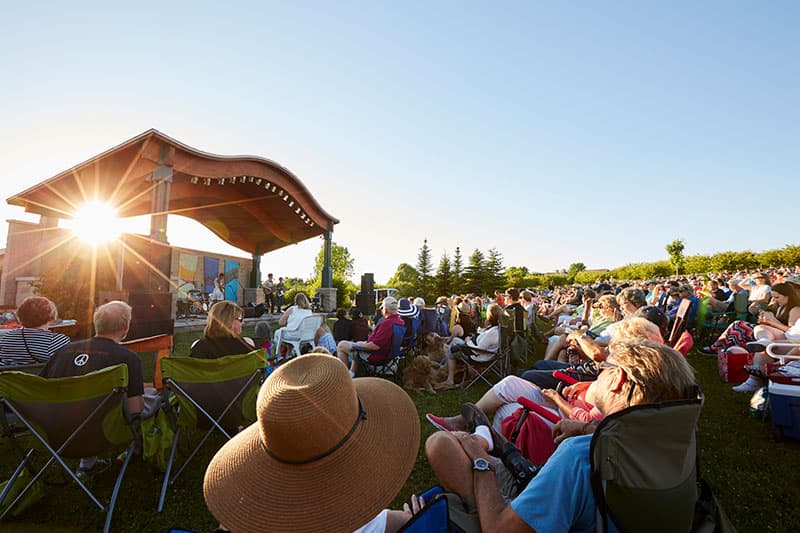 A large crowd enjoys a live performance at an outdoor venue under a clear blue sky. A large crowd enjoys a live performance at an outdoor venue under a clear blue sky.