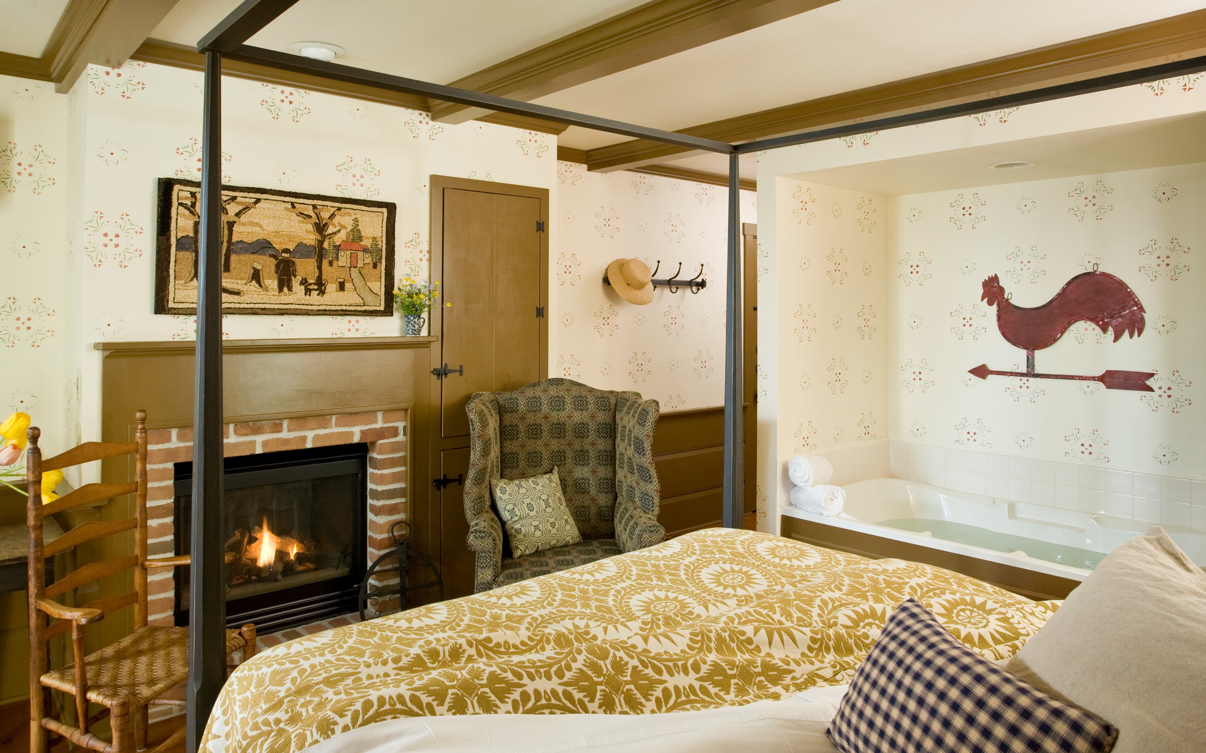 Cozy bedroom with a fireplace, patterned bedspread, and vintage decor, including a whimsical rooster on the wall.