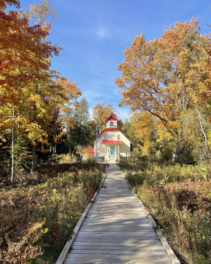 A charming house with a red roof surrounded by colorful autumn trees and a wooden path.