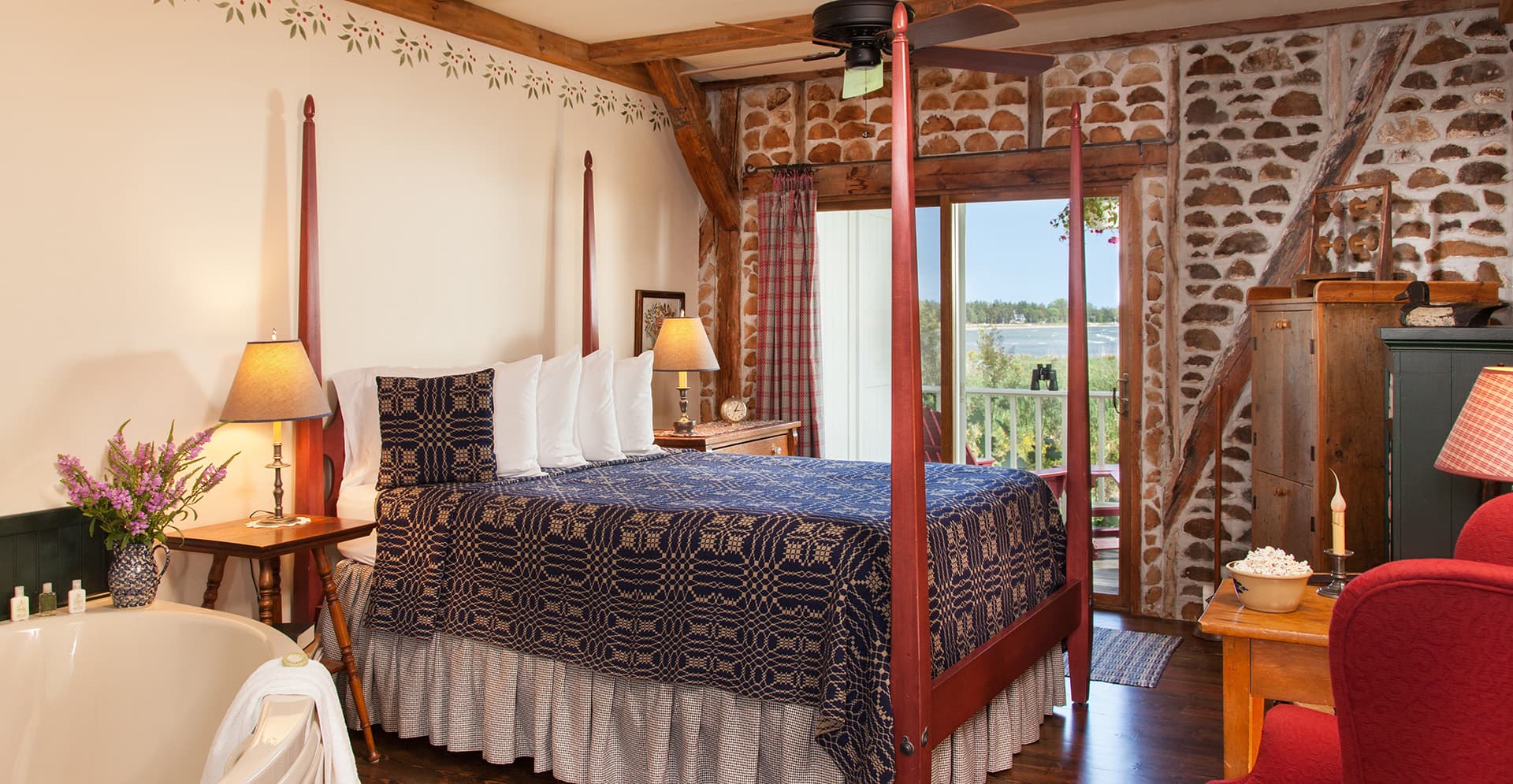 A cozy bedroom featuring a four-poster bed, a freestanding tub, and large windows with scenic views.