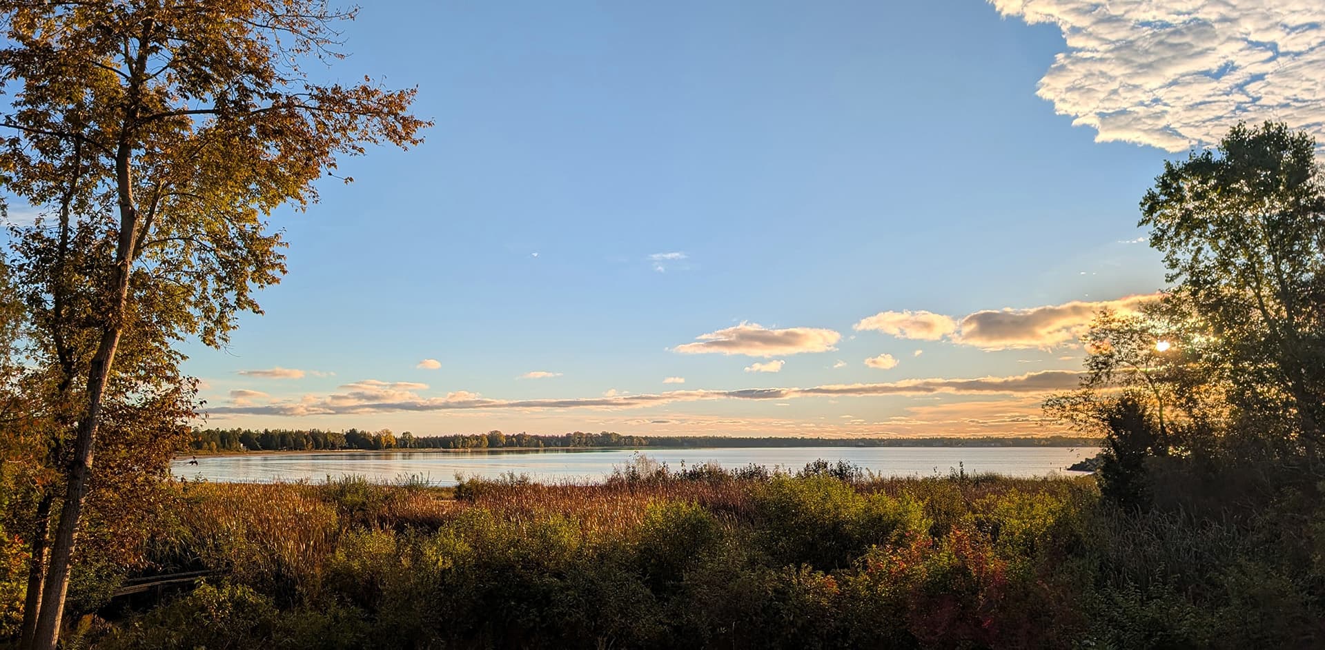 A serene landscape featuring a calm lake bordered by trees and colorful foliage under a clear blue sky.