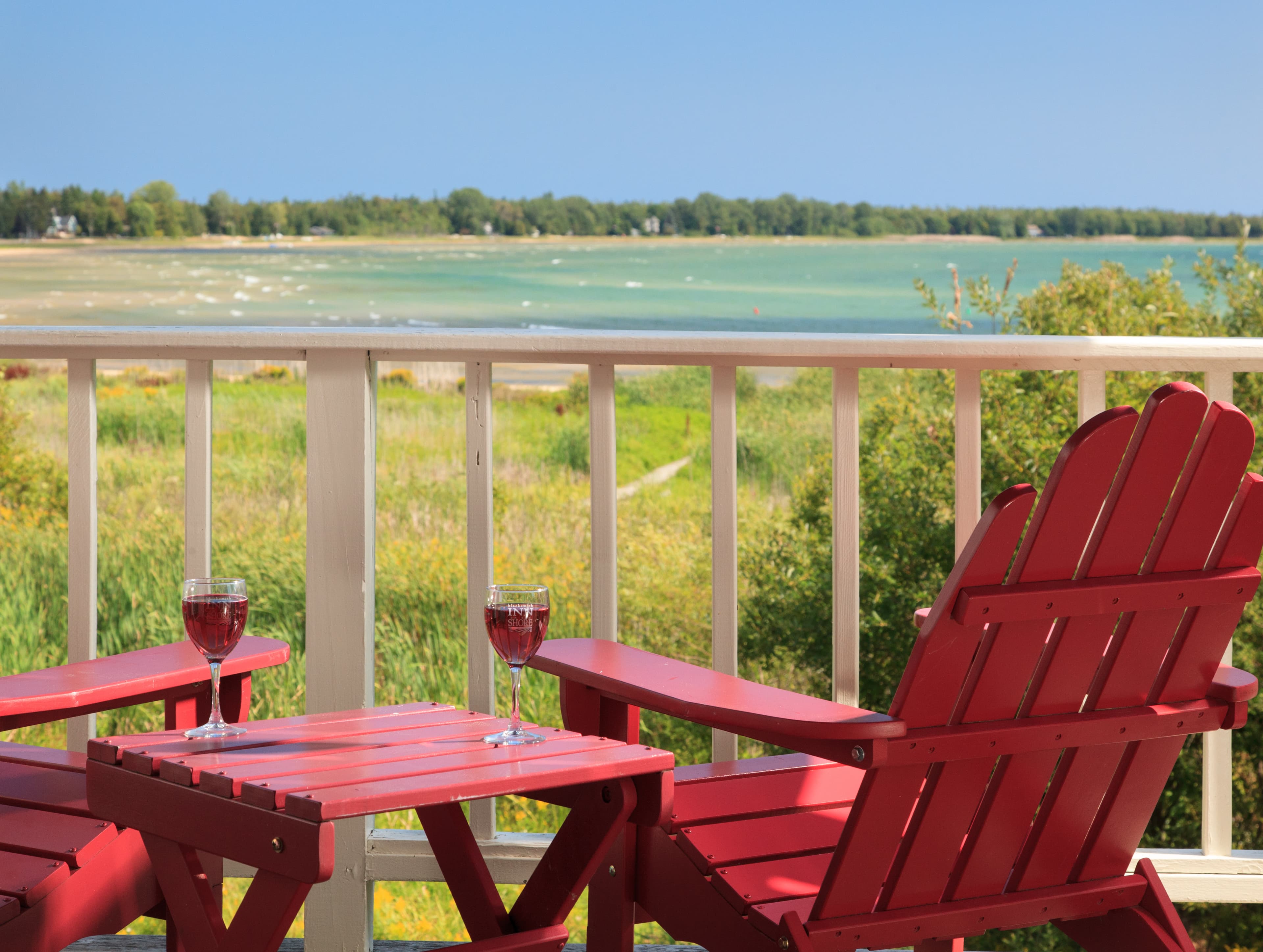 Two red chairs and a small table with glasses of wine overlook a peaceful lakeside view.