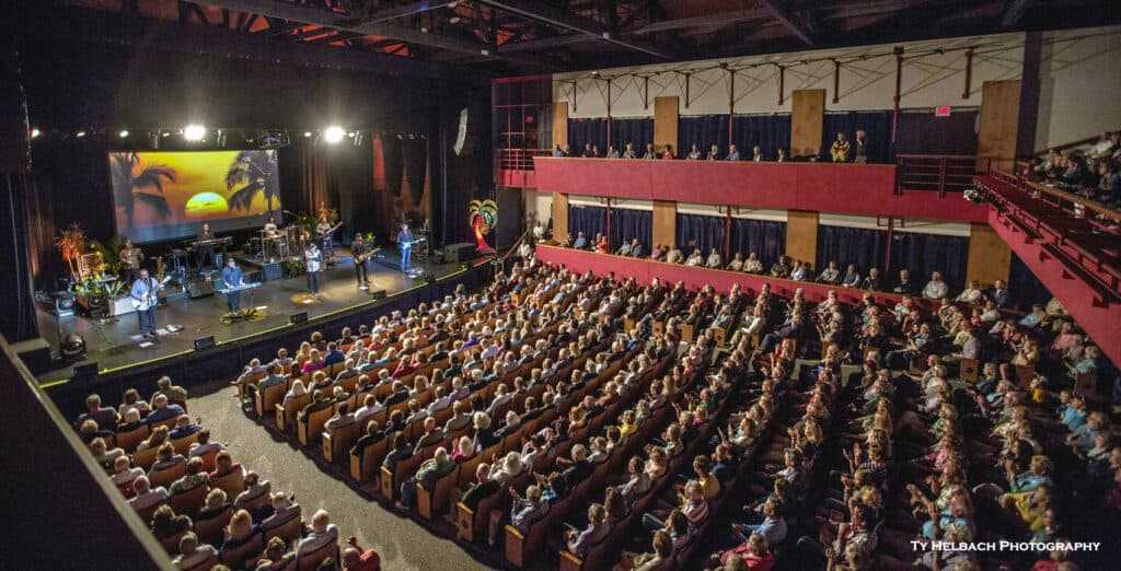 A large audience watches a live performance on stage in a theater.