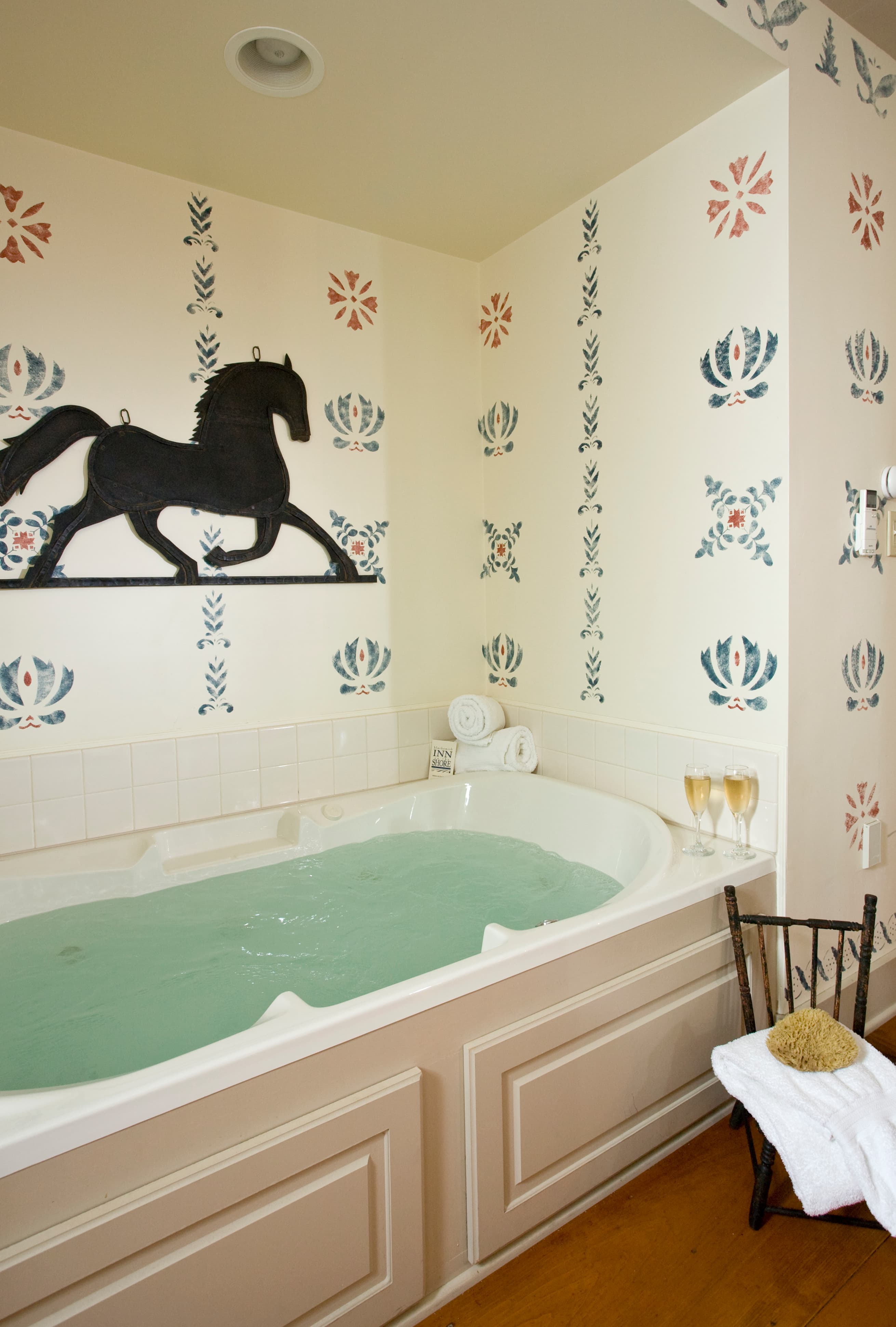 A cozy bathroom features a jetted tub, decorated walls, plush towels, and two glasses of champagne.
