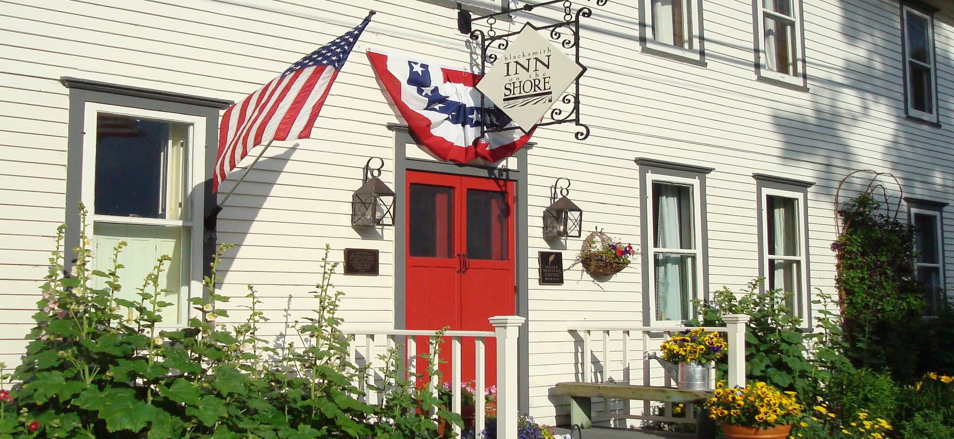 Charming inn with a red door, American flag, and vibrant flower beds.